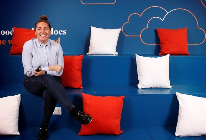 Ultimate Finance employee sitting on blue, orange and white stalls and smiling at the camera