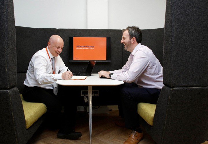 Two Ultimate Finance team members having a discussion in a cubicle