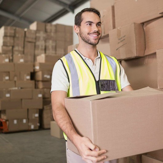 A smiling man carrying trade goods in a warehouse against a backdrop of packages